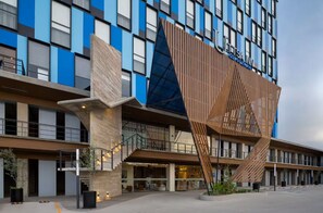 A modern hotel with a distinctive facade featuring blue and brown panels, a prominent wooden slatted structure, and a visible entrance with a staircase. - Tryp By Wyndham Ciudad Guzman Uttsa (Zapotlán el Grande)
