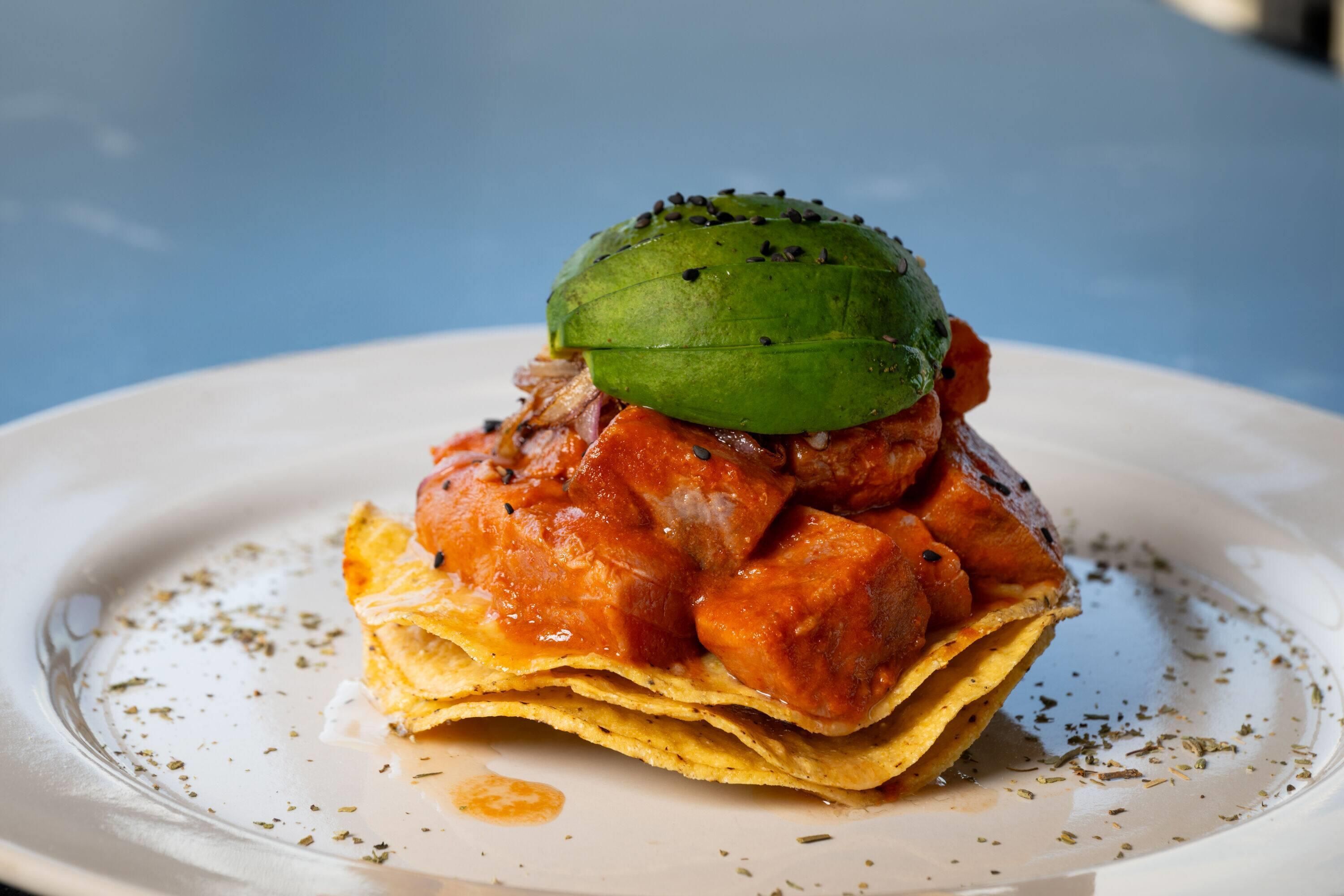 Un plato con un alimento que consiste en una base de tortilla cubierta con un vegetal verde y salsa roja.
