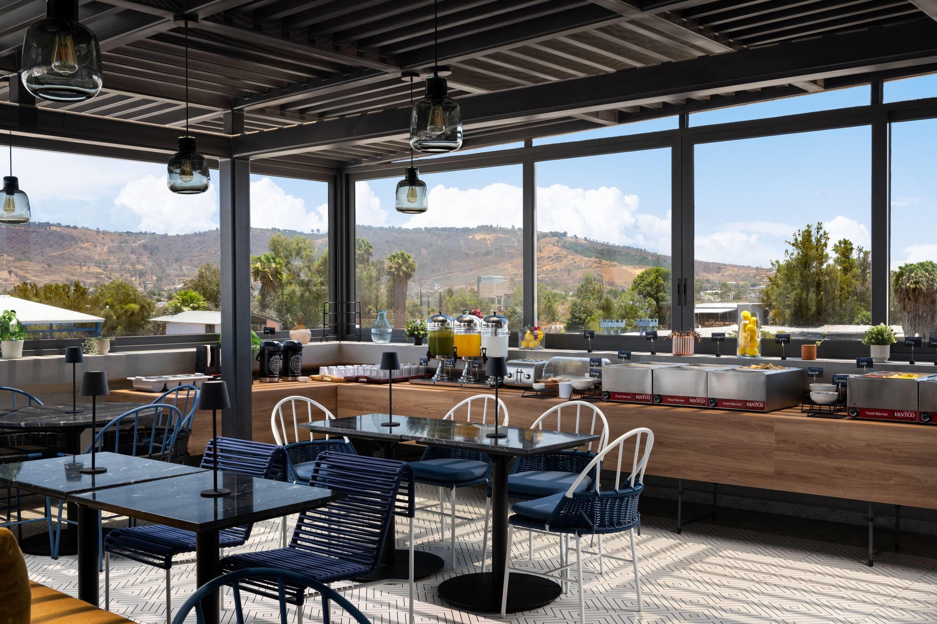 Un espacio moderno para comer al aire libre con ventanas amplias, diversas opciones de asiento y vistas a las colinas.