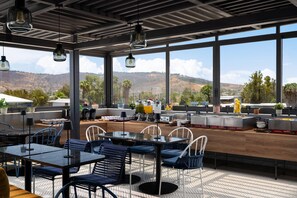 Un'area pranzo esterna moderna con ampie finestre, diverse opzioni di seduta e vista sulle colline.