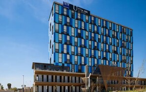 Ein modernes Hotelgebäude mit einer blau und schwarzen Fassade, zahlreichen Fenstern und einem Schild mit der Aufschrift 'UTTSA INN'.