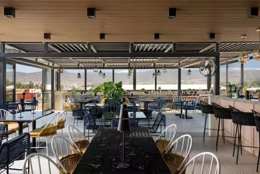 Un área de comedor al aire libre con mesas y sillas, un bar y vistas a la montaña.