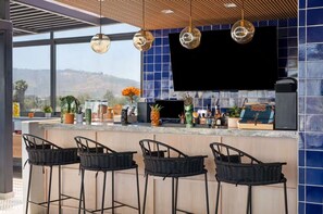 A modern bar area with a large TV, bar stools, and various bottles and plants on the counter. - Tryp By Wyndham Ciudad Guzman Uttsa (Zapotlán el Grande)