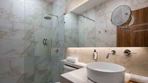 Um banheiro moderno com box revestido em azulejo de mármore, pia redonda e toucador de madeira.