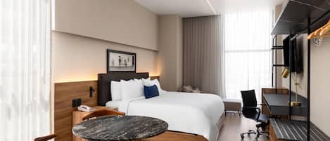 Una habitación de hotel moderna con cama, escritorio, silla, mesita y televisor.