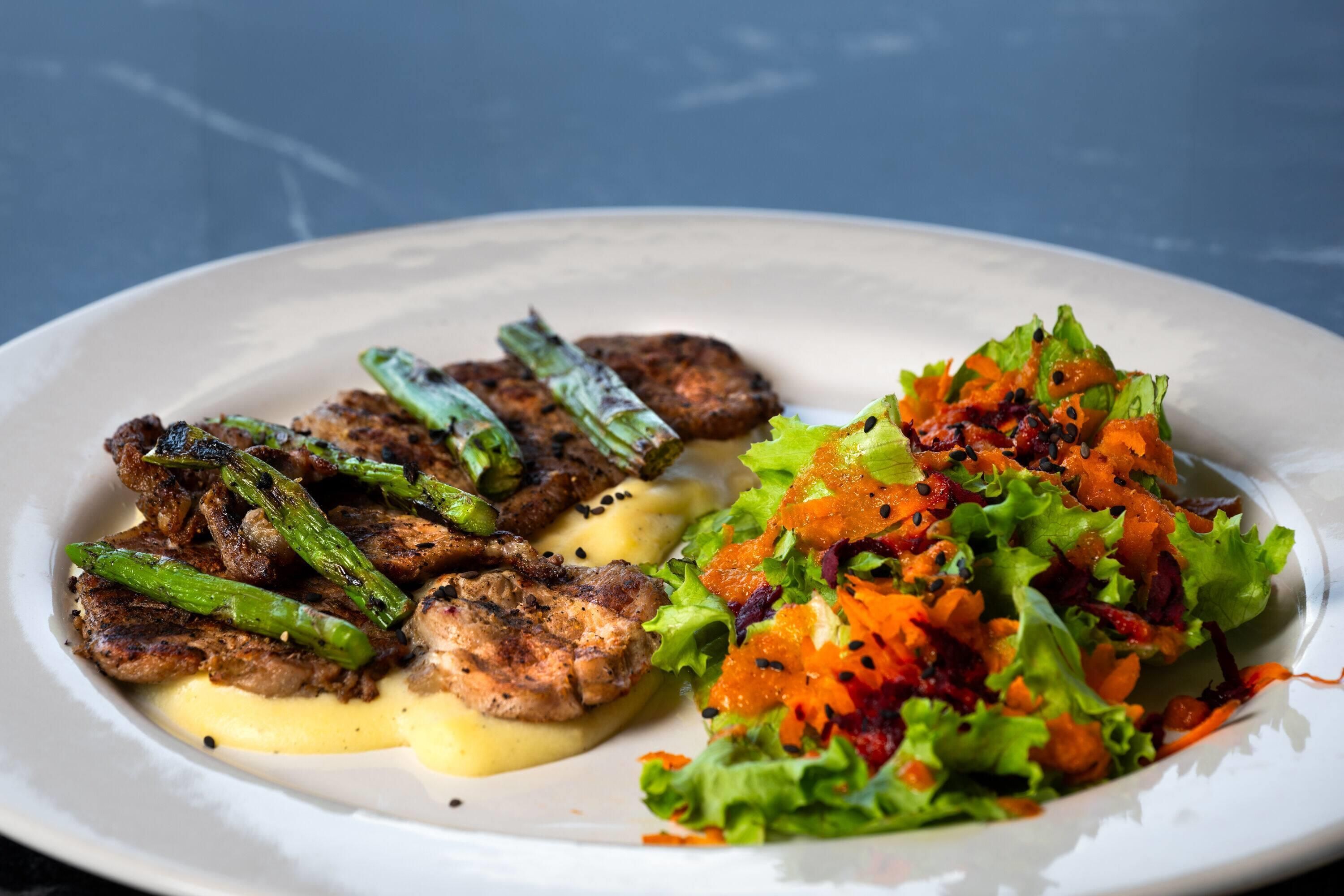 Un plato de comida con carne a la parrilla, espárragos y ensalada.