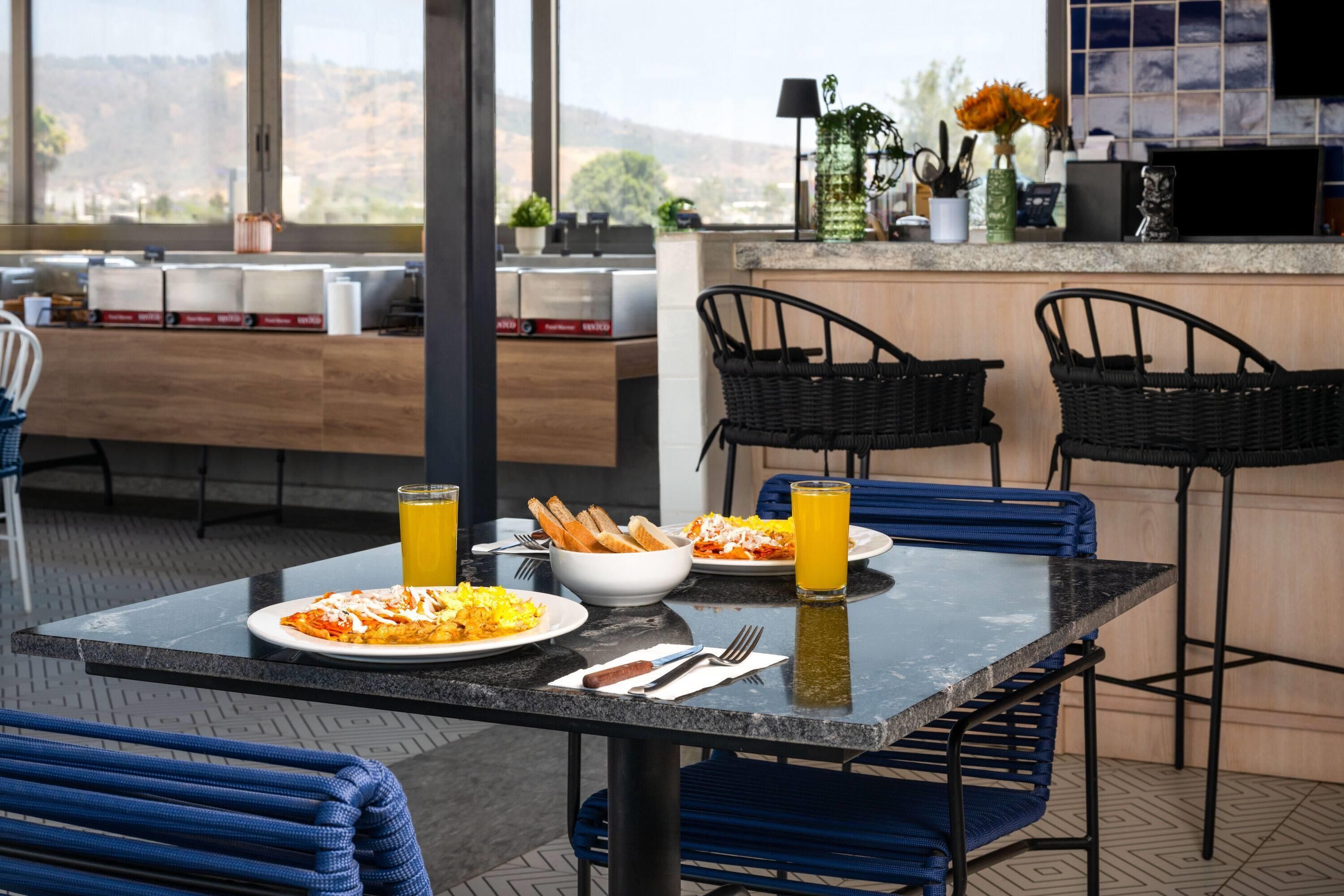 Comedor con una mesa dispuesta para dos personas, mostrando platos de comida y bebidas, y vistas al exterior.