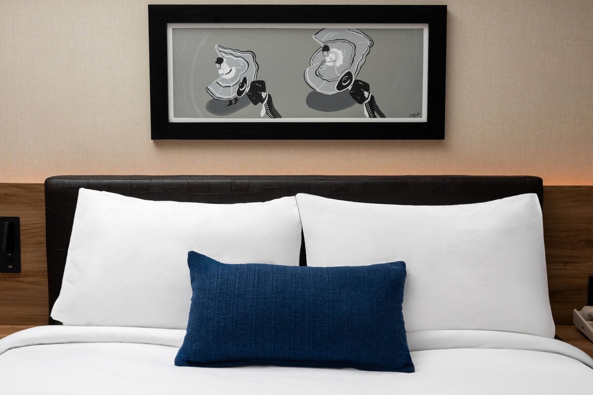 A neatly made bed with white and blue pillows, a framed artwork above it, and a wooden headboard.