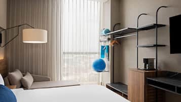 Una habitación de hotel moderna con una cama grande, un escritorio con cafetera, una pelota de ejercicios colgante y un televisor montado en la pared.
