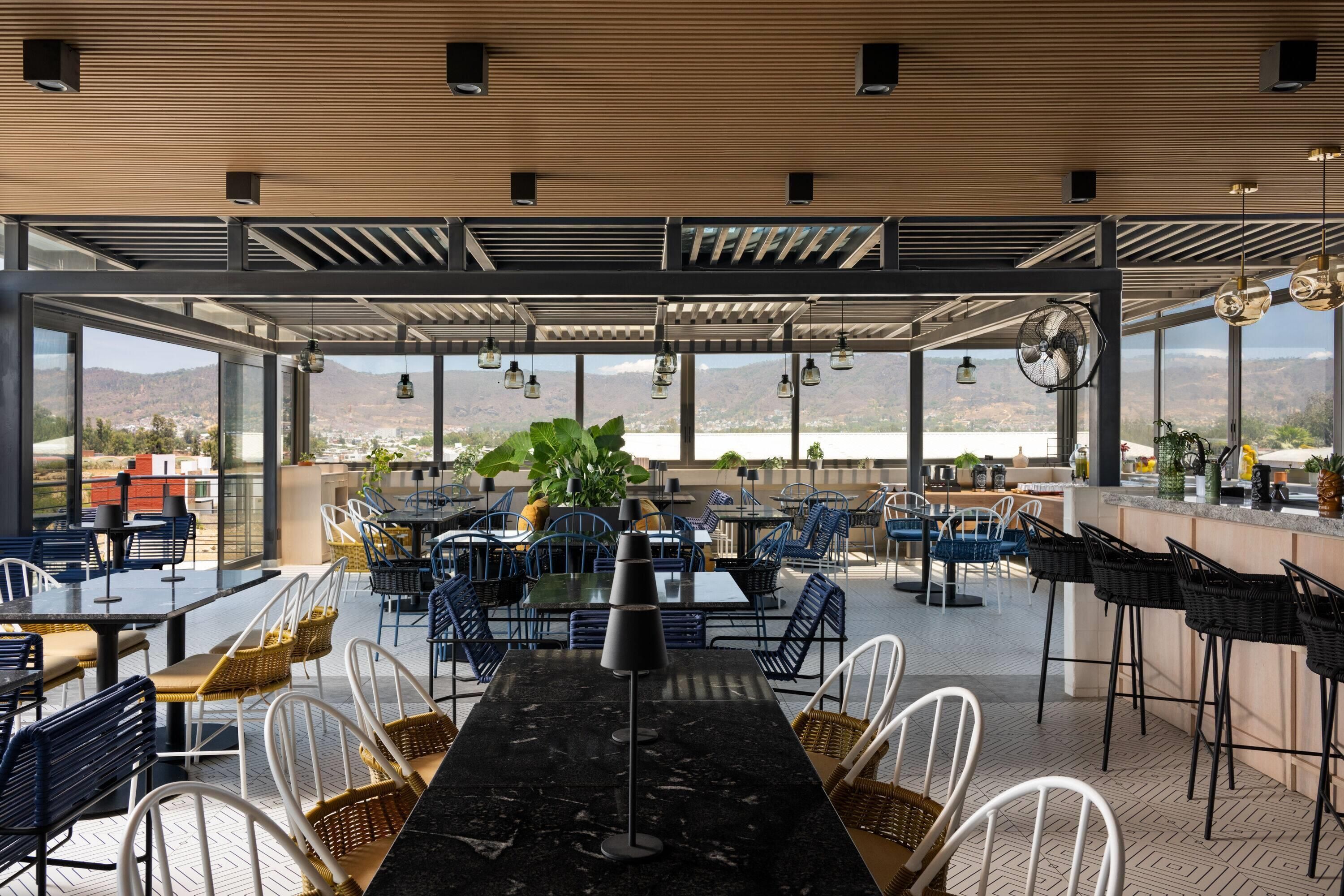 An outdoor dining area with tables and chairs, large windows, and a view of the landscape.