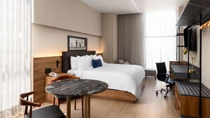 Une chambre d’hôtel moderne équipée d’un grand lit, d’un bureau, d’une chaise, d’une petite table et d’un téléviseur.