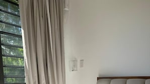 A neatly made bed with a striped basket on it, a window with curtains, and a plain wall with a light switch. - Peaceful Apartment in Palmas del Mar (Palmas del Mar)