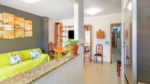Cozinha moderna com bancada de granito, um sofá verde vibrante e um espaço de jantar com cadeiras de madeira e uma mesa.