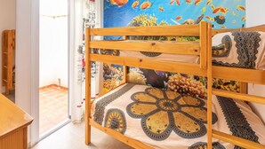 Uma cama beliche com colcha estampada, um mural de peixes na parede e vista do exterior através de uma porta.