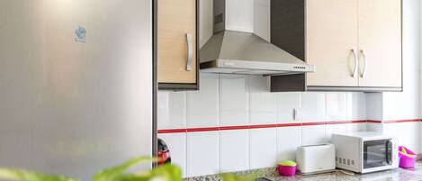 A kitchen with a stainless steel refrigerator, a microwave, a toaster, and a washing machine.
