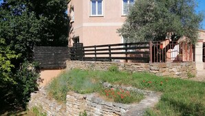 A stone-walled building with a flat roof, a wooden fence, and a stone pathway leading to a gate.