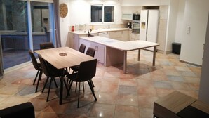 A modern kitchen with a dining area, featuring a large island, built-in appliances, and a sliding glass door leading to an outdoor area.