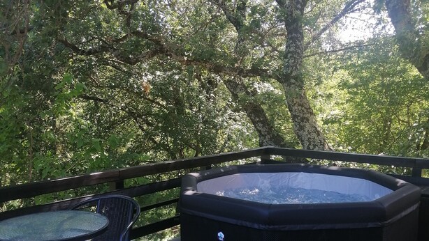 A hot tub on a patio with a table and chairs, surrounded by trees.