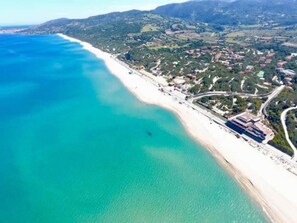 An aerial view of a coastal area with a beach, roads, and buildings.