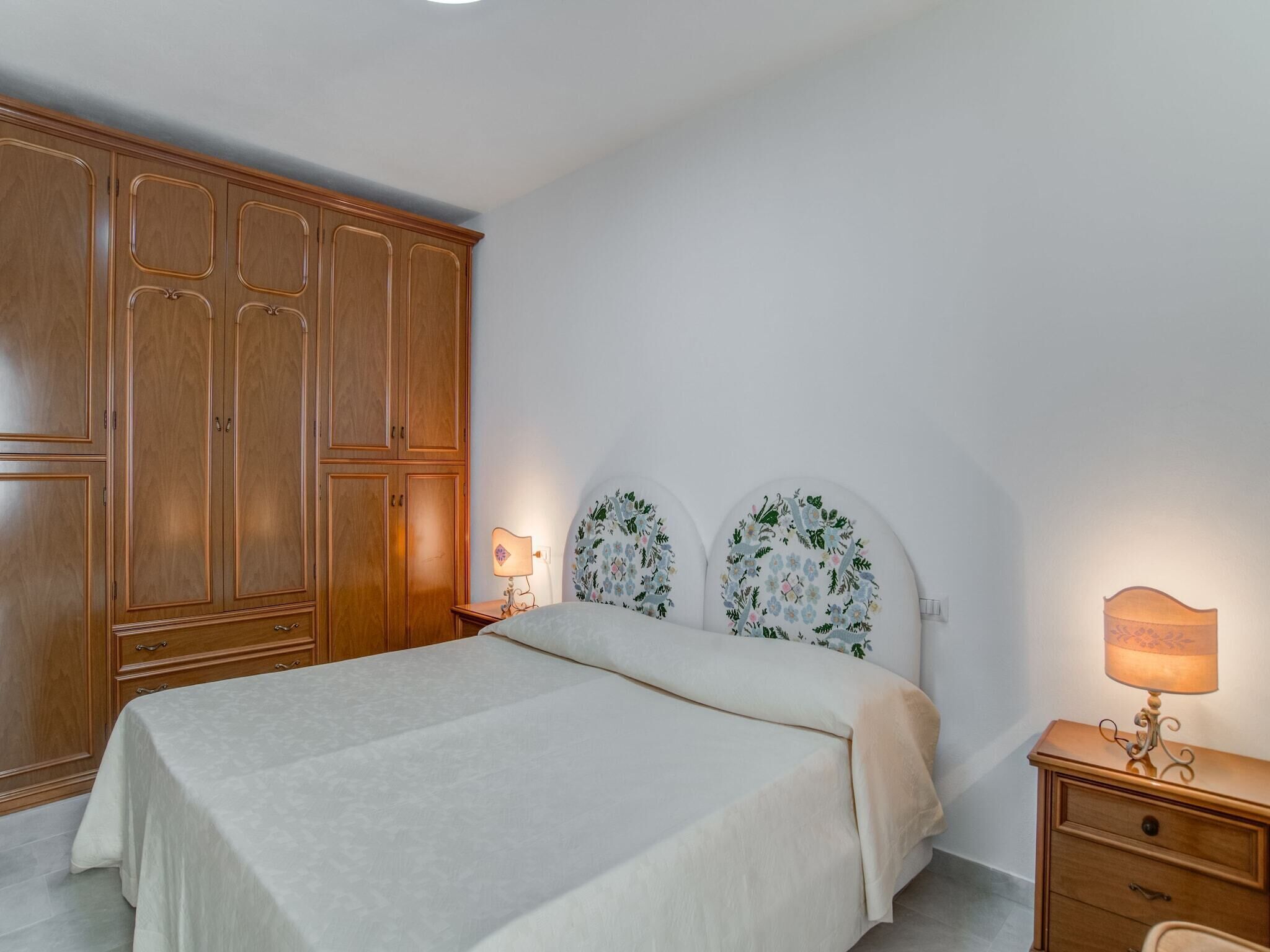 A bedroom with a bed, wooden wardrobe, bedside tables, and wall-mounted lamps.