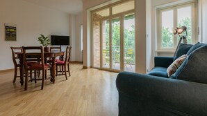A spacious living room with a wooden dining table, chairs, a blue sofa, a TV, and a balcony with glass doors. - Casa Cinema by Wonderful Italy (Turin)
