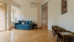 A spacious living area with a blue sofa, wooden flooring, and a door leading to another room. - Casa Cinema by Wonderful Italy (Turin)