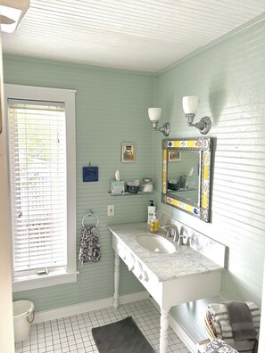 A bathroom with a white vanity, a large mirror with a decorative frame, a towel rack, and a window with blinds. - Spacious Home with Water Views (Cedar Key)