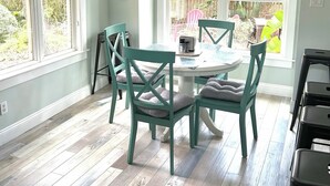 Un coin repas avec une table ronde et quatre chaises, de grandes fenêtres donnant sur l’extérieur et une bouche d’aération au plafond.