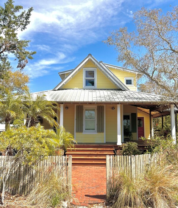 A yellow house with a red brick entrance, a wooden fence, and a clear blue sky. - Spacious Home with Water Views (Cedar Key)