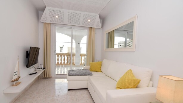 Una sala de estar moderna con un sofá blanco, una mesa de centro de vidrio y un televisor de pantalla plana sobre un mueble blanco.
