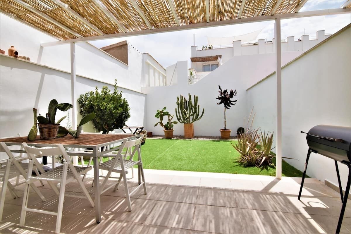 Un espace patio aménagé avec une table et des chaises, entouré de plantes en pot et d’un barbecue.