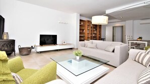 A modern living room with a flat-screen TV, a glass coffee table, a sofa, a bookshelf, and a dining area. - CA NA MARONA - Dúplex al centre del poble (Colonia de Sant Pere)