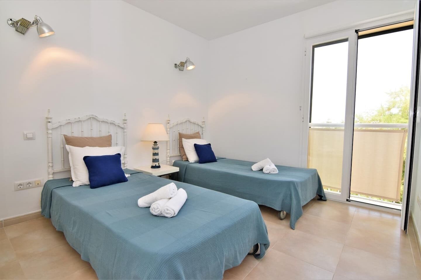 A hotel room with two beds, each with a headboard, a nightstand, a lamp, and a pair of towels.