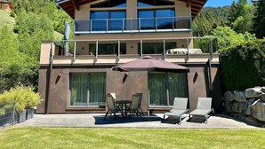 Ein modernes, zweistöckiges Haus mit Balkon, großen Fenstern und einer Sitzgelegenheit im Freien.