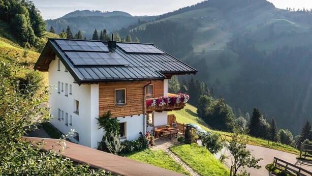 Una cabaña con techo inclinado, paneles solares y un balcón de madera con flores.