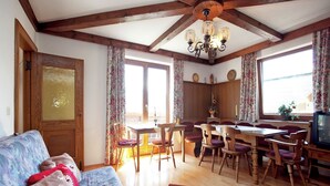 Una sala de estar acogedora con techo de madera, comedor con mesa y sillas, y un televisor sobre un mueble de madera.