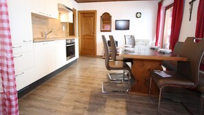 A kitchen with white cabinets, a wooden dining table, and a TV on the wall.