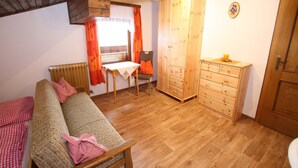 A cozy room with a wooden sofa, a small table with a chair, a wooden wardrobe, and a radiator.
