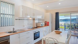 A modern kitchen with white cabinets, a built-in oven, and a dining area with a table and chairs.