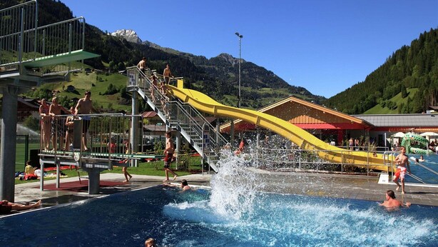 A swimming pool with a water slide, surrounded by mountains and a clear sky.