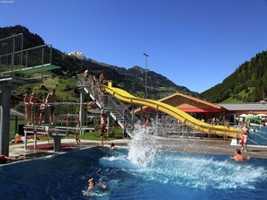 Una piscina con tobogán de agua, rodeada de montañas y un cielo despejado.