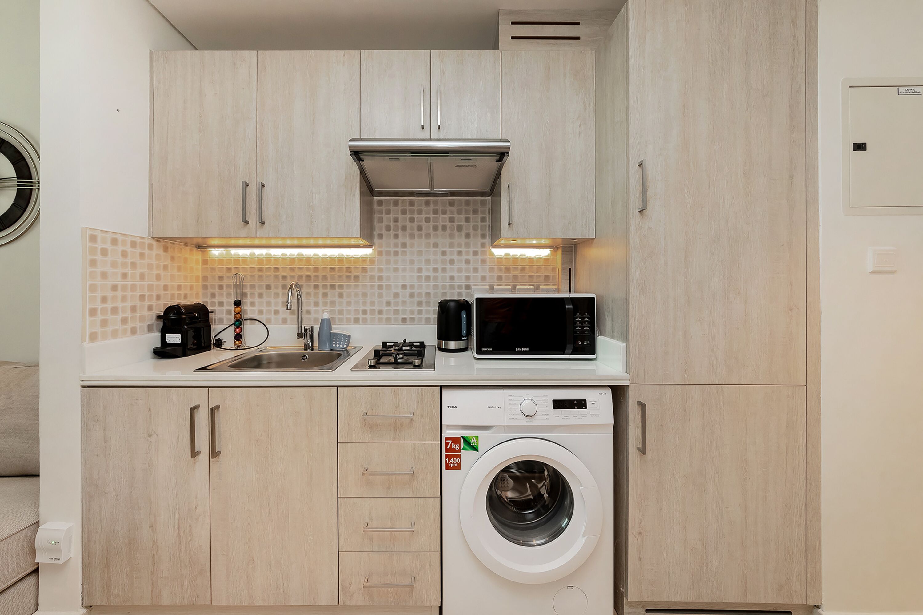 A compact kitchen with a washing machine, microwave, and coffee maker.