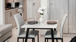 A modern dining area with a white table, grey upholstered chairs, and a vase with white flowers.