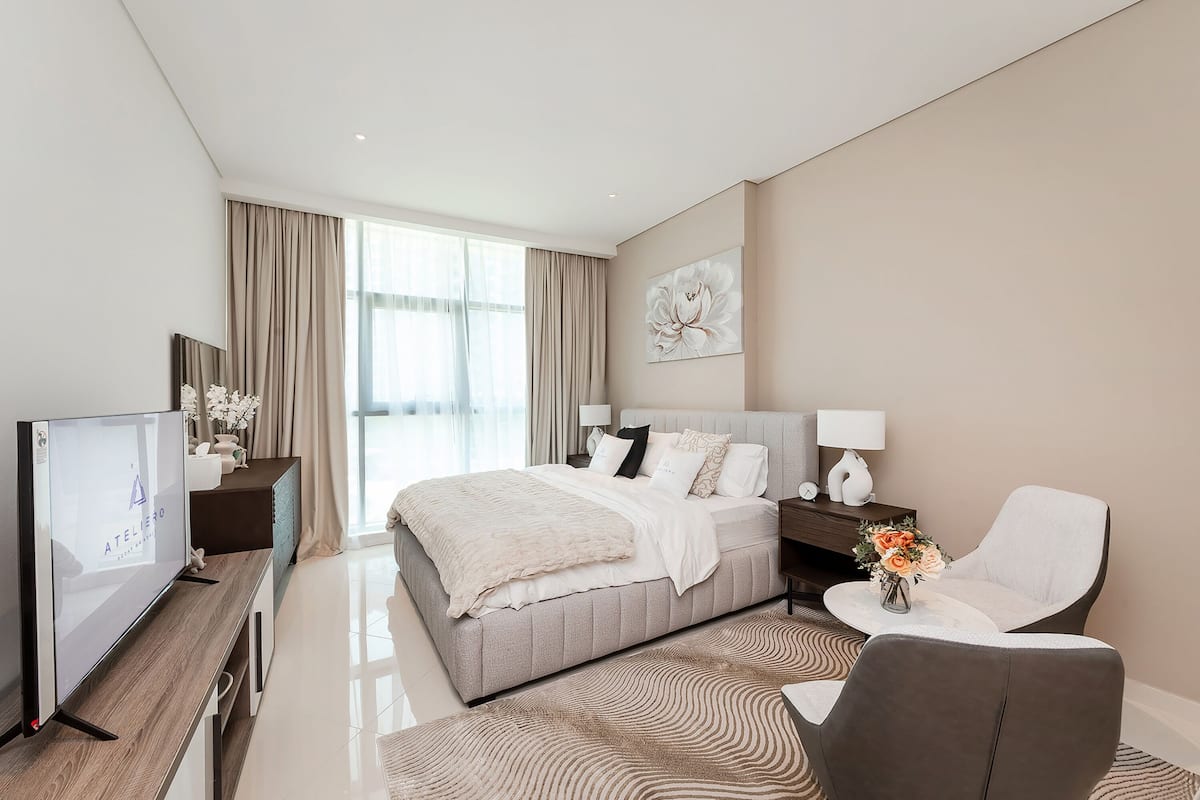 A modern hotel room with a large bed, a flat-screen TV, a desk with a lamp, and a chair.