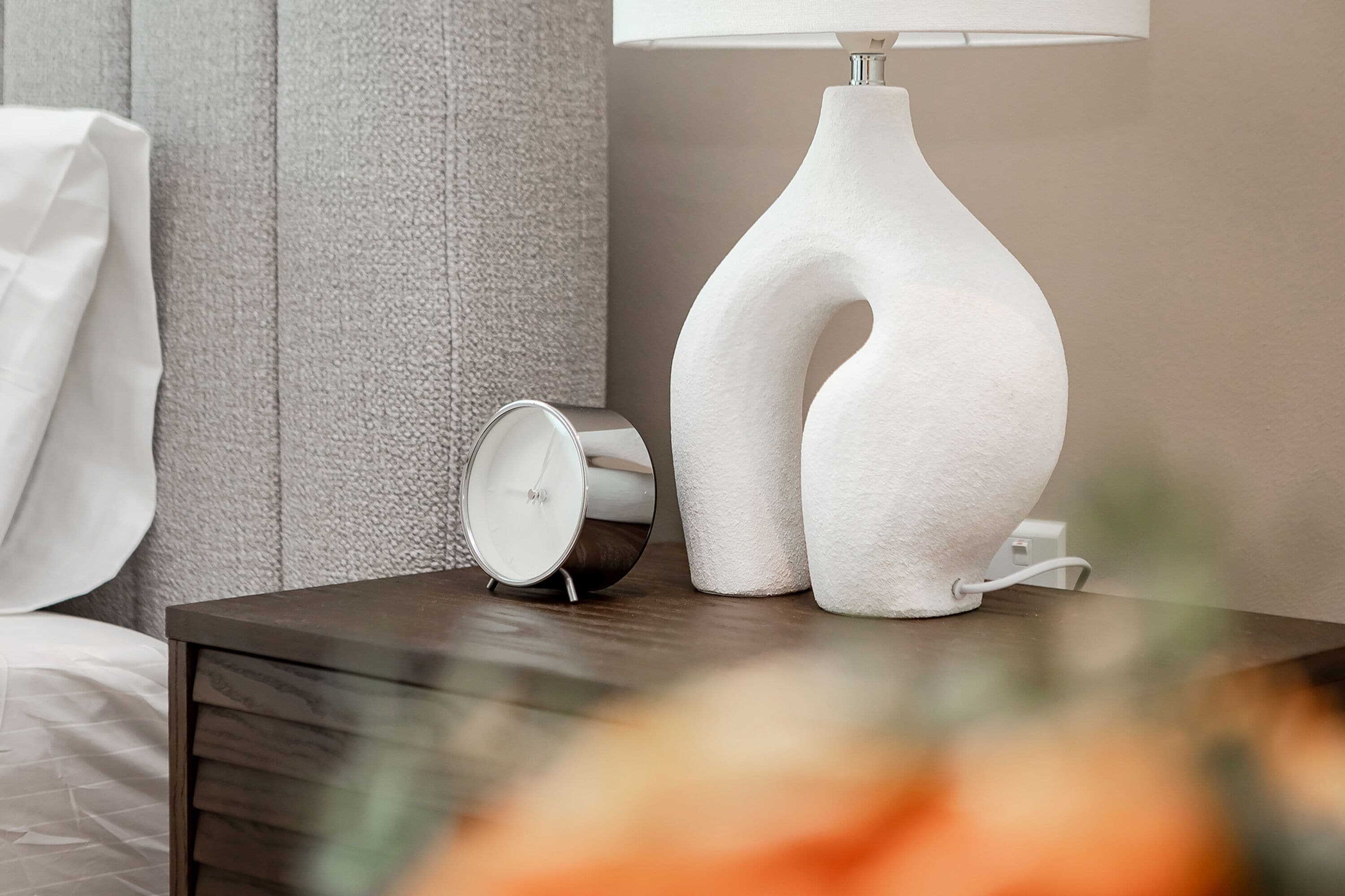 A modern bedside table with a white lamp and a small analog clock.
