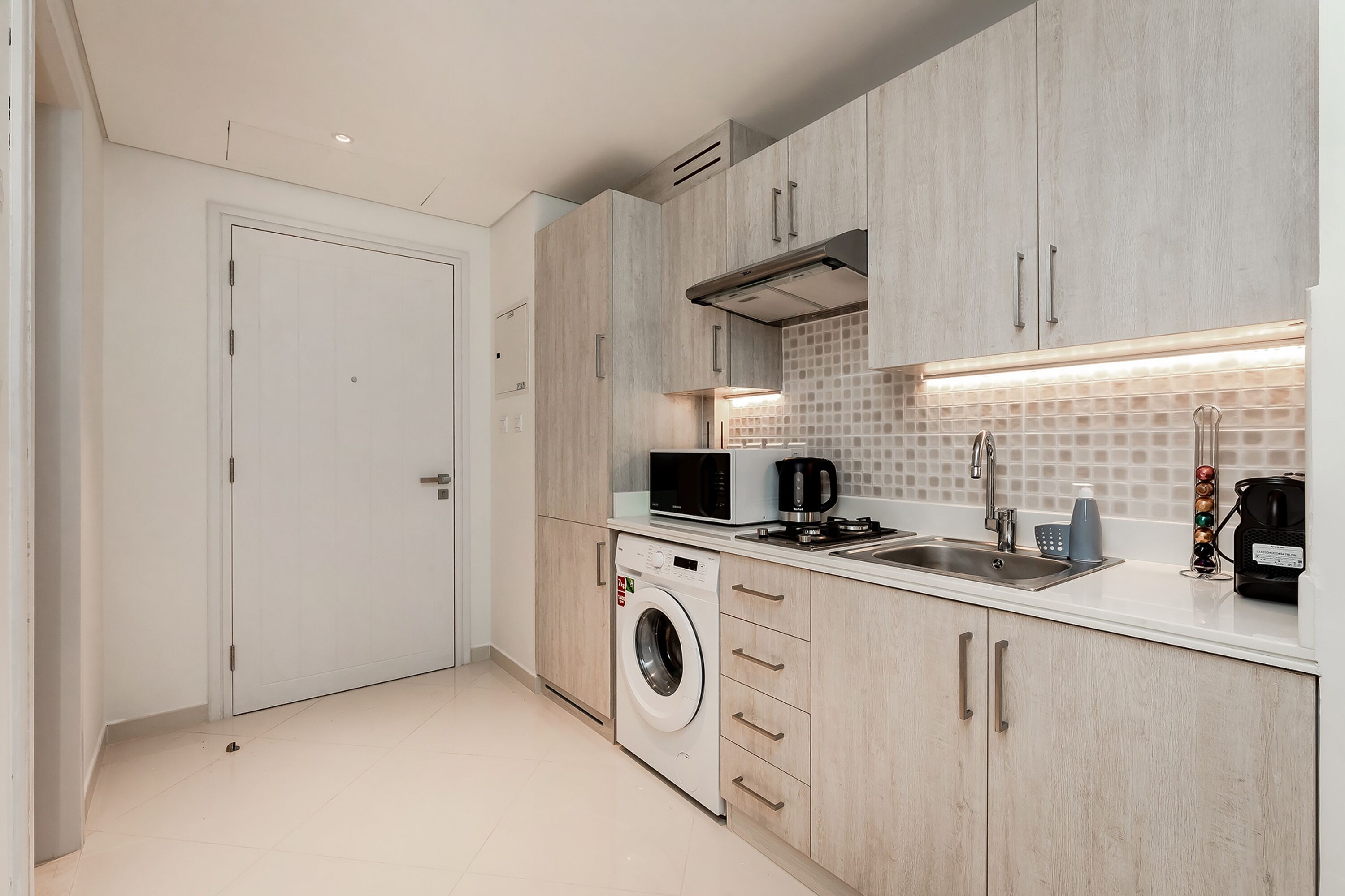 A modern kitchen with a washing machine, microwave, and coffee maker.