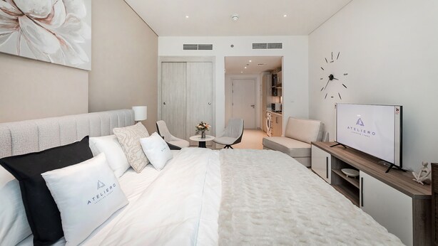 A modern hotel room with a large bed, a TV, a seating area, and a bathroom visible through an open door.