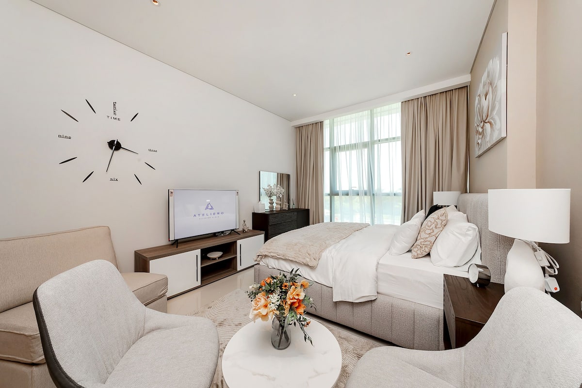 A modern hotel room with a bed, a TV, a sofa, a coffee table, and a clock on the wall.