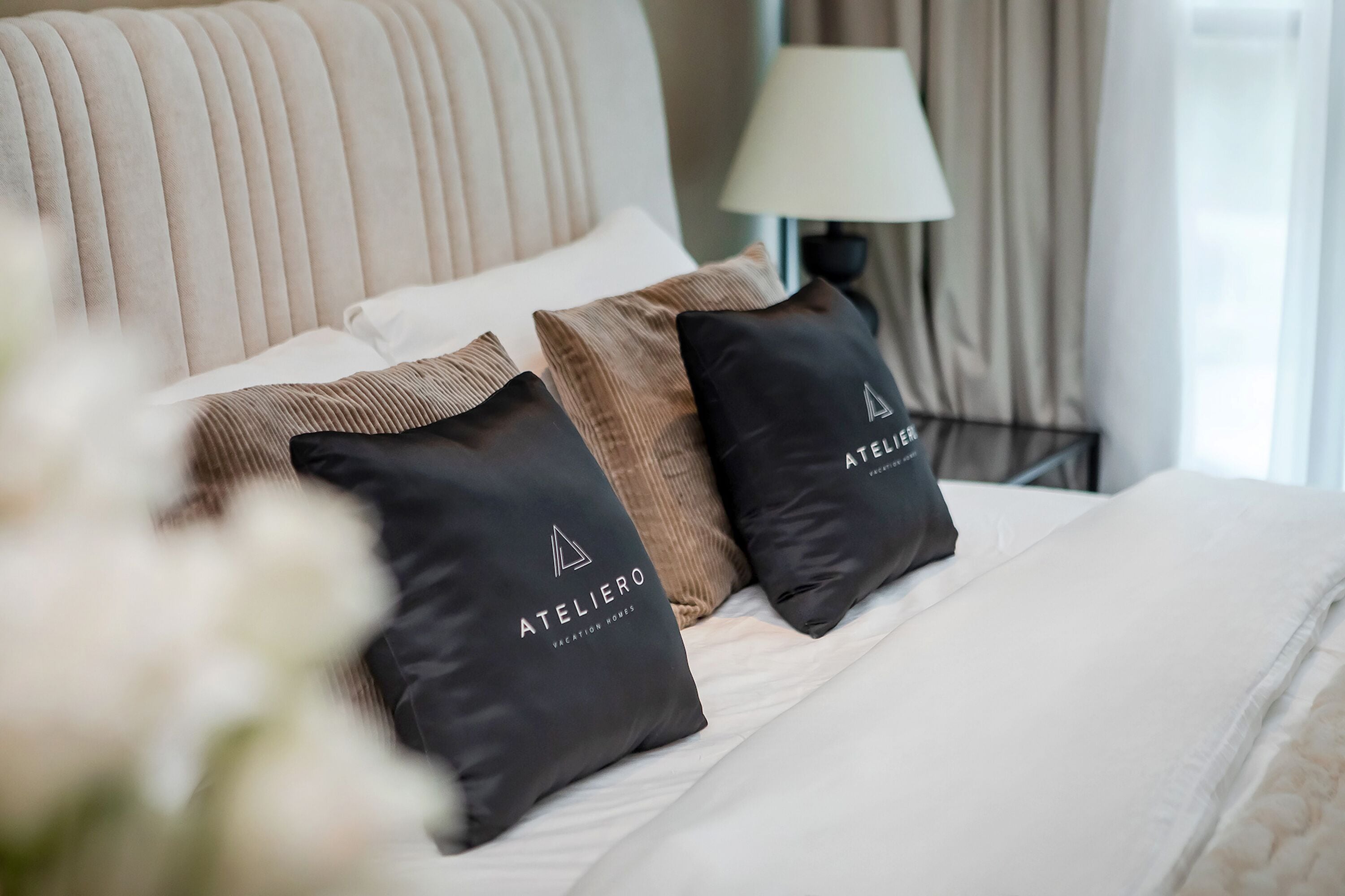 A neatly made bed with two pillows, one with a logo and text, and a lamp in the background.