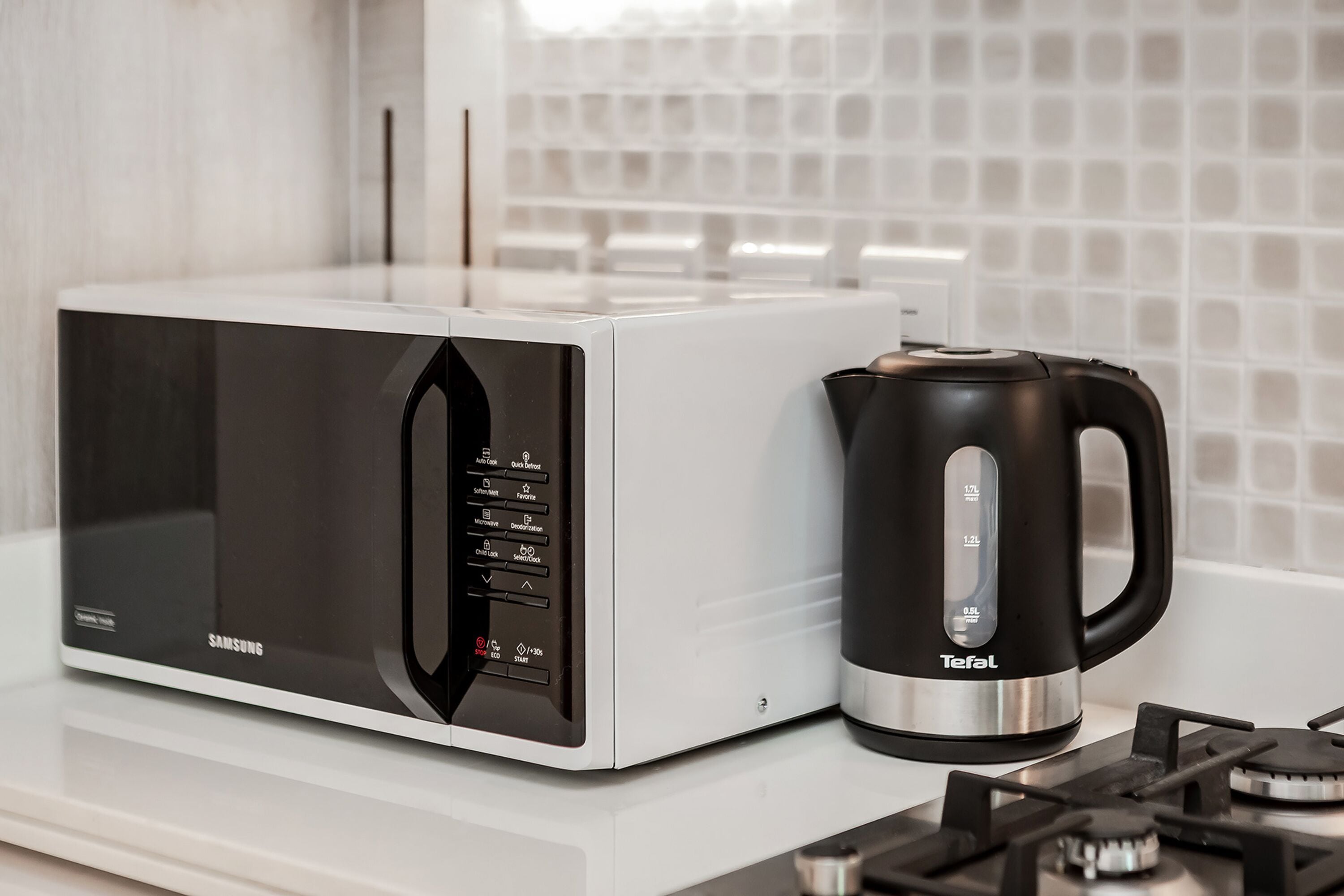 A modern kitchen with a white microwave and a black coffee maker on a white countertop.